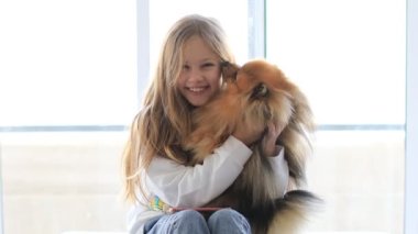 Evdeki küçük sevimli kız evcil köpeğini kucağına alıp oynuyor.