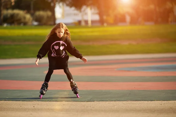 Маленькая счастливая забавная девчонка на роликовых коньках в парке, учится кататься на роликах под открытым небом. Детский отдых на свежем воздухе. Активный спорт для детей дошкольного возраста — стоковое фото