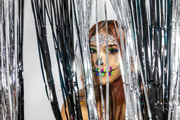 Cadılar bayramı partisi için makyajlı, gümüş ve siyah şeritlerin arkasına saklanan genç bayanın yakın çekimleri..