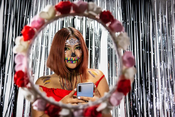 Cadılar bayramı makyajlı bir kadının elinde bir çiçek ve cep telefonu çemberinin arkasında yakın plan fotoğrafı.