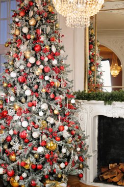 Şöminenin yanında parlayan sihirli ağaç. Noel ağacı olan bir Noel evi. Çam dallarında asılı kırmızı ve beyaz toplar. Tuğla duvar arka planında şenlik ışıkları. Yeni yıl konsepti.