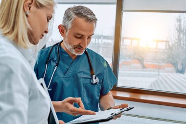 İki doktor tıbbi belgeleri okuyor ve modern bir hastanede bir hastanın teşhisini tartışıyorlar. Görüntüyü kapat.