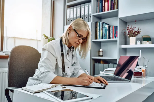 Médica Séria Usando Laptop Escrevendo Notas Diário Médico Sentado Mesa — Fotografia de Stock