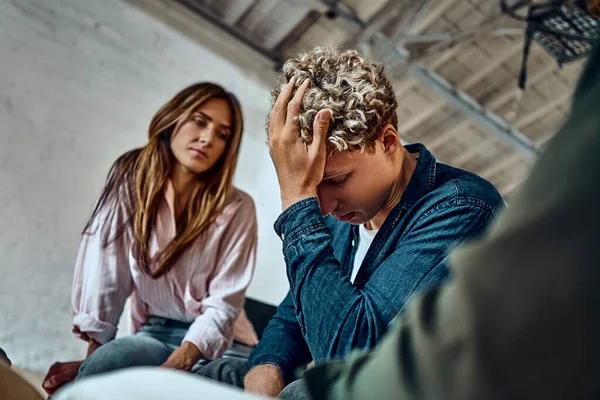 Helping with loss and psychological problems, alcohol and drug addiction. Diverse people sitting in circle, supporting and comforting crying distraught group member in therapy session at rehab center. Selective focus. Close up view