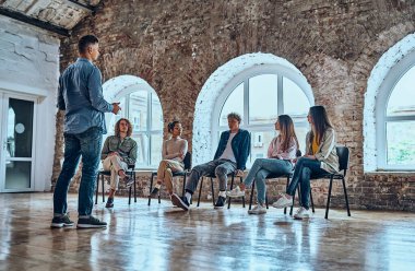 Kendine güvenen erkek lider, koç bir grup ofis çalışanıyla konuşuyor, astlarıyla iyi sohbet ediyor, beyin fırtınası yapıyor, iş stratejilerini, fikirleri, takım oluşturma faaliyetlerini tartışıyor. Düşük açı görünümü