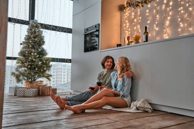 Modern mutfakta yerde oturmuş kırmızı şarap içen ve birlikte güzel vakit geçiren genç ve güzel bir çift..