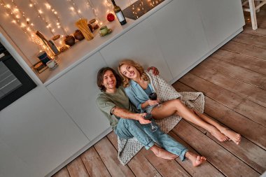 Evdeki mutfak zemininde oturmuş şarap içen genç ve güzel bir çiftin manzarası. Noel zamanı.