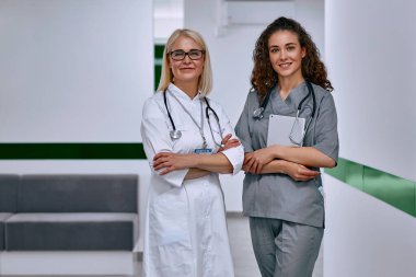 Kliniğin koridorundaki iki kadın doktor kameraya bakıyorlar. Sağlık hizmetleri.
