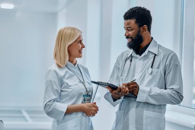 Beyaz önlük giymiş iki doktor hastane koridorunda konuşup gülüyor..