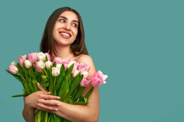 Mavi arka planda elinde bir buket beyaz ve pembe lale tutan güzel bir genç kadının portresi. Bahar ve güzellik kavramı.