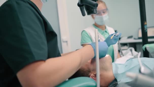 Male Dentist Uses Microscope While Treating Patient Clinic Female Assistant — Stock Video
