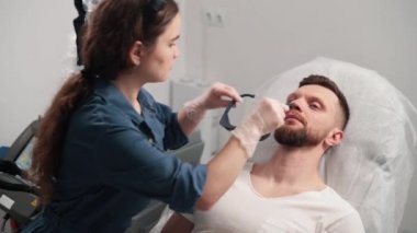 Profesyonel kozmetik uzmanı güzellik salonundaki adama koruyucu gözlük takıyor. Yakın plan..