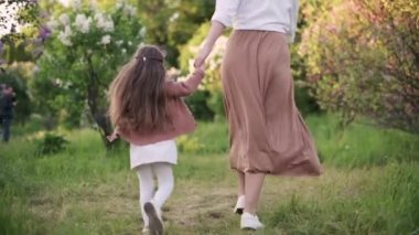 Anne ve kızı çimenlerde koşuyorlar. Bacaklara yakın çekim, dikiz manzarası. Aile boş zamanlarını parkta geçirir. Yavaş çekim.