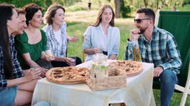 Bir grup arkadaş dışarıda birlikte dinleniyorlar. Genç insanlar masada oturuyor, sohbet ediyor ve gülüyorlar..