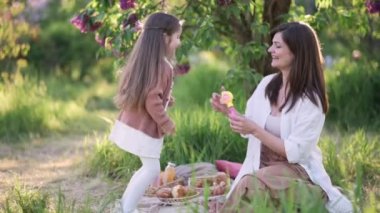 Anne ve kızı eğleniyor. Dört yaşındaki kızı onu elleriyle yakalarken genç bir kadın sabun köpüğü üflüyor. Yavaş çekim.