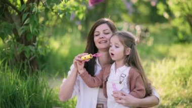 Anne ve kızı eğleniyor. Genç ve çekici bir kadın dört yaşındaki kızıyla dışarıda baloncuk yapıyor..