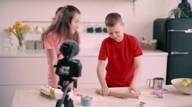 Oğlan ve kız evde yemek blogu kaydediyor. Çocuk merdaneyle kurabiye için hamur topluyor. Sabit çekim.