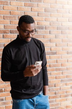 Afrikalı adam akıllı telefon kullanıyor. Elinde cep telefonu olan gözlüklü bir gencin portresi..