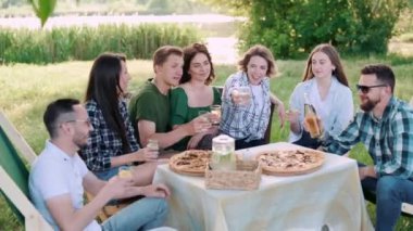 Bir grup arkadaş dışarıda birlikte dinleniyorlar. Genç neşeli insanlar kadehleri tokuşturup gülüyor..