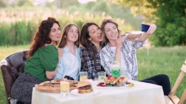 Neşeli arkadaşlar doğada selfie çekerler. Bir grup çekici genç kadın bir fotoğraf için komik suratlar çiziyor..