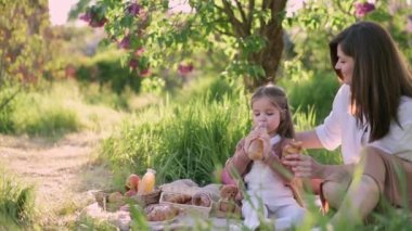 Anne ve kızı piknikte. Küçük kız şişeden meyve suyu içiyor..