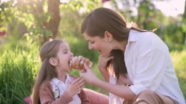 Anne ve kızı piknikte. Annem küçük kızına kruvasan veriyor..