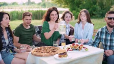 Bir grup arkadaş dışarıda birlikte dinleniyorlar. Genç bir kadın soğuk limonatayı bardaklara dolduruyor..