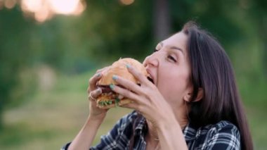 Genç, çekici, aç bir kadın büyük bir hamburgeri ısırıyor. Kapat..