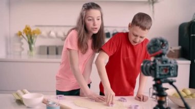 Boy and girl recording culinary blog at home. Children make cookie blanks using a mold.