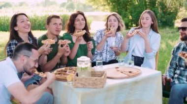 Bir grup arkadaş dışarıda birlikte dinleniyorlar. Gençler masada oturmuş, sohbet ediyor ve pizza yiyorlar..