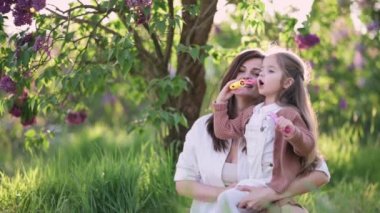 Anne ve kızı eğleniyor. Genç ve çekici bir kadın dört yaşındaki kızıyla dışarıda baloncuk yapıyor..