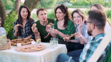 Bir grup arkadaş dışarıda birlikte dinleniyorlar. Gençler masada oturmuş, eğleniyor, konuşuyor ve yemek yiyorlar..