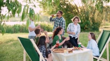 Bir grup arkadaş dışarıda birlikte dinleniyorlar. Genç neşeli insanlar kadehleri tokuşturup gülüyor..