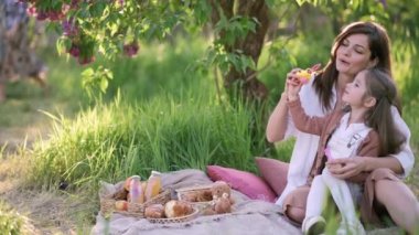 Anne ve kızı eğleniyor. Genç ve çekici bir kadın dört yaşındaki kızıyla dışarıda baloncuk yapıyor..