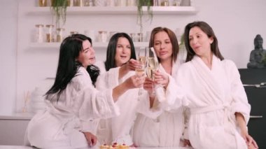 A group of women spend leisure time. Young attractive females in bathrobes drink champagne and chat merrily at home.