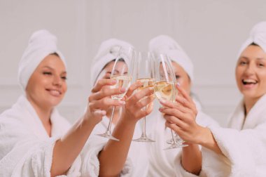 A group of women at a party. Girlfriends in bathrobes clink glasses, close-up of hands.