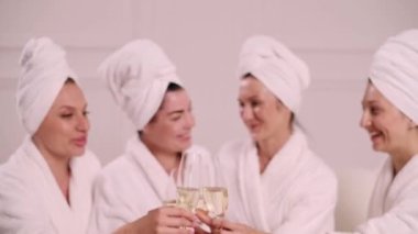 A group of women spend leisure time. Young attractive females in bathrobes drink champagne and chat merrily.