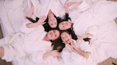 Girlfriends are having fun. Four young females in bathrobes lie on the bed and have fun. View from above.