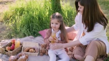 Anne ve kızı piknikte. Küçük kız şişeden meyve suyu içiyor..