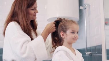 Annem kızıyla ilgileniyor. Genç beyaz kadın banyoda şirin küçük kızlarının saçlarını örüyor..