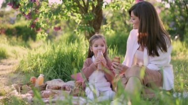Anne ve kızı piknikte. Küçük kız şişeden meyve suyu içiyor..