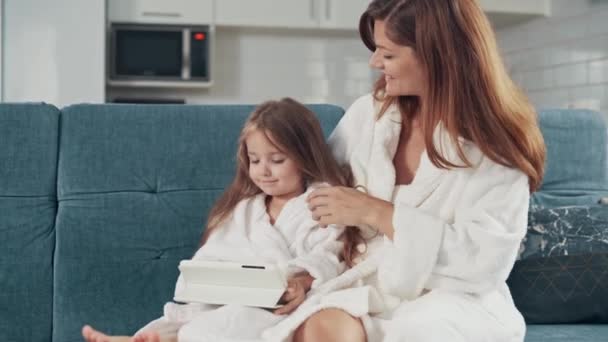 年轻漂亮的女人和她的学龄前女儿在家里的沙发上用平板电脑 — 图库视频影像