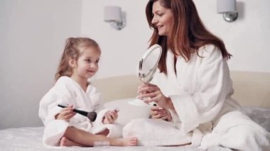 Sevimli anaokulu kızı makyaj yapmayı annesinden öğreniyor. Çocuk aynada kendine bakıyor..