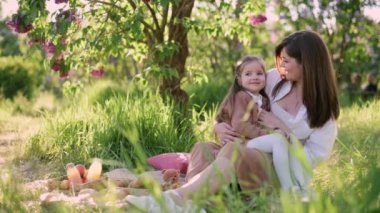 Genç bir anne, çiçek açan bir ağacın yanında küçük tatlı bir kızı kollarında tutar. Sevgi dolu bir annenin kollarında dört yaşında bir kız..