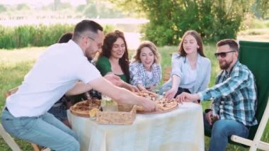 Bir grup arkadaş dışarıda birlikte dinleniyorlar. Gençler masada oturmuş, sohbet ediyor ve pizza yiyorlar..
