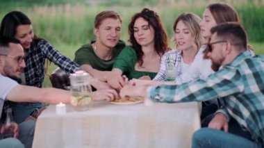Bir grup arkadaş dışarıda birlikte dinleniyorlar. Gençler masada oturmuş, eğleniyor, konuşuyor ve yemek yiyorlar..