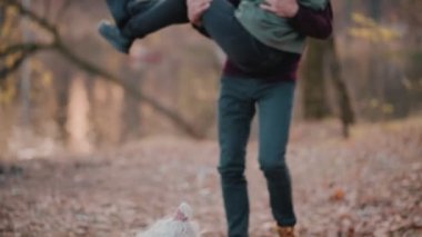 Komik kıvırcık köpek sahiplerinin yanında oturuyor. Neşeli Adam kız arkadaşını sonbahar parkında kollarında döndürür..