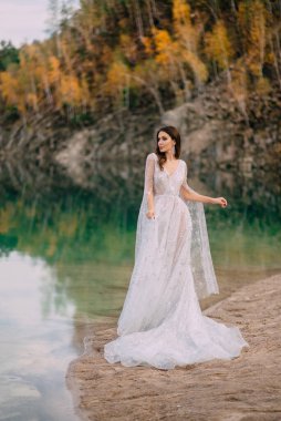 Genç bir gelin, sonbahar ormanıyla çevrili güzel bir gölün kıyısında duruyor..