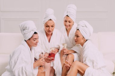A group of women spend leisure time. Four Young attractive women in bathrobes look at the smartphone screen and smile.