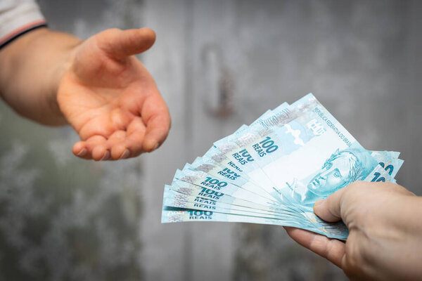 Brazilian money, a file of banknotes of one hundred Reais passed from hand to hand, economic and business concept